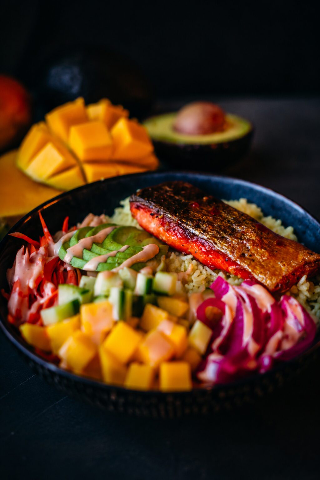 Juicy salmon on top of rice with a chili lime glaze served alongside avocado, mango, carrots, pickled red onion, and spicy mayo