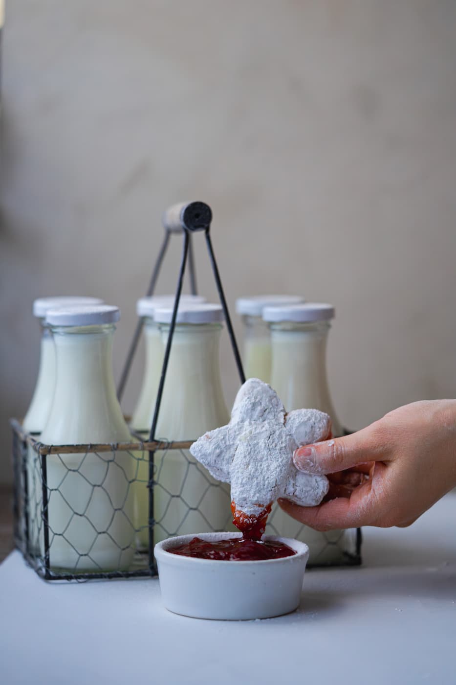 kelly-jean-TclQHtlkzRc-unsplash A close-up shot of a single, pillowy soft New Orleans homemade beignet being dipped into red fruit jam, heavily coated in a layer of white powdered sugar.