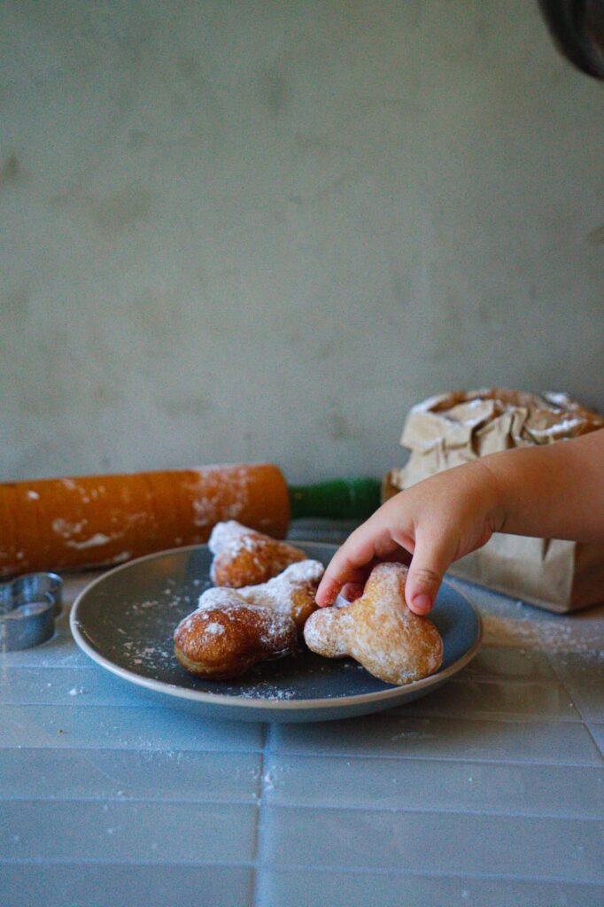 A close-up of a child picking up a Mickey-shaped powdered sugar beignet.