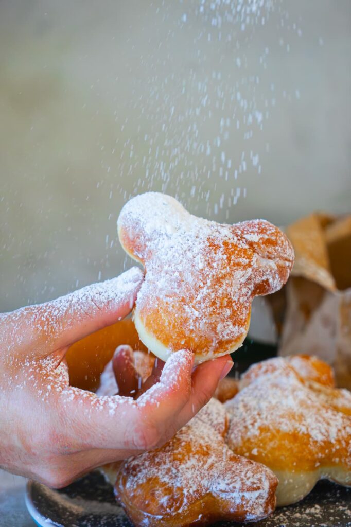 Close up of a mickey shaped homemade beignet being dusted with powdered sugar