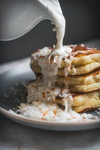 Fluffy Coconut Ricotta pancakes stack with haupia syrup being poured over them