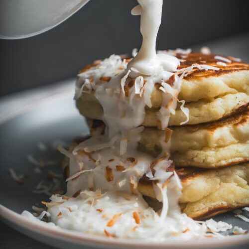 Fluffy Coconut Ricotta pancakes stack with haupia syrup being poured over them