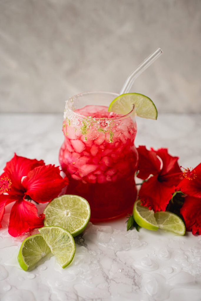 Glass of vibrant red honey lime hibiscus iced tea with fresh lime slices and ice cubes.