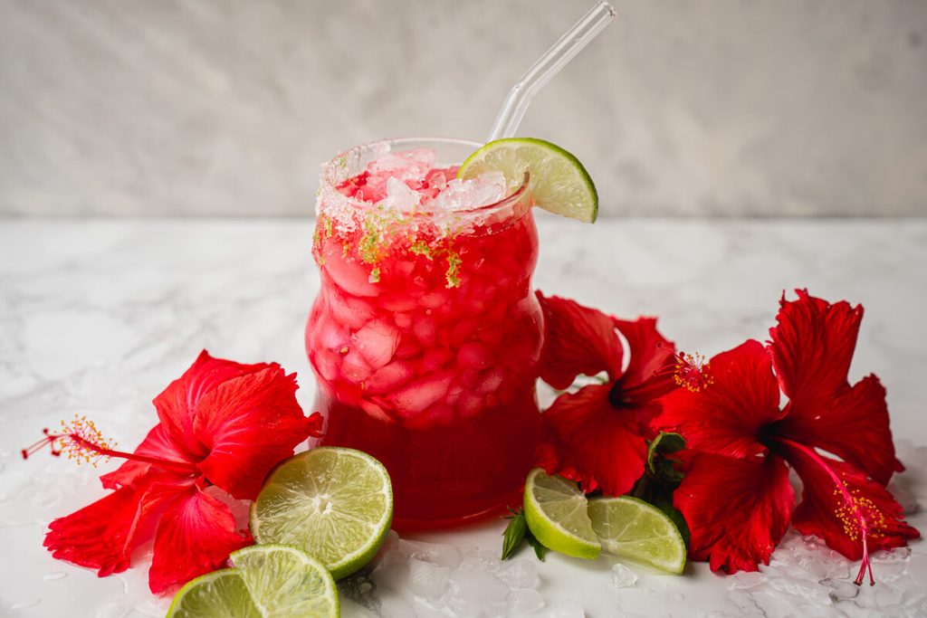 Glass of vibrant red honey lime hibiscus iced tea with fresh lime slices and ice cubes.