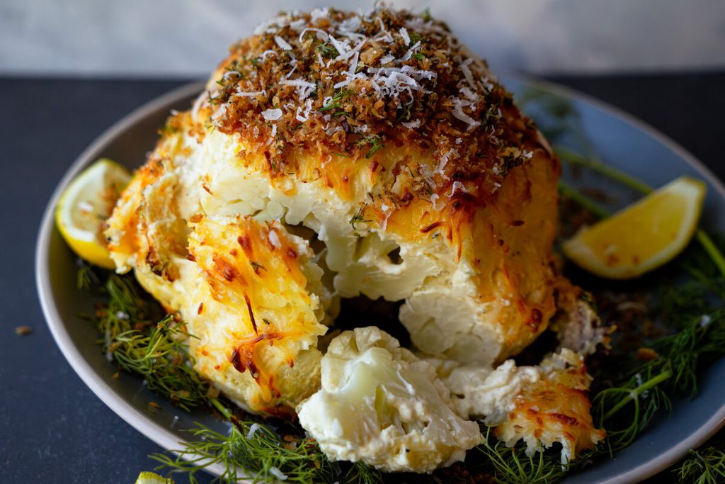 cheesy whole roasted cauliflower served with dill, lemon wedges, and topped with crispy panko herb breadcrumbs
